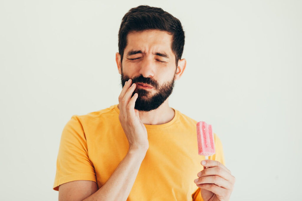 Man with sensitive teeth touching his jaw due to tooth pain caused by a cold popsicle