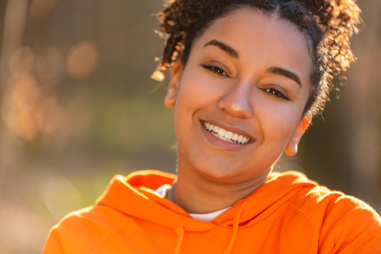 Attractive biracial young woman wearing orange hoodie shares her pretty smile 