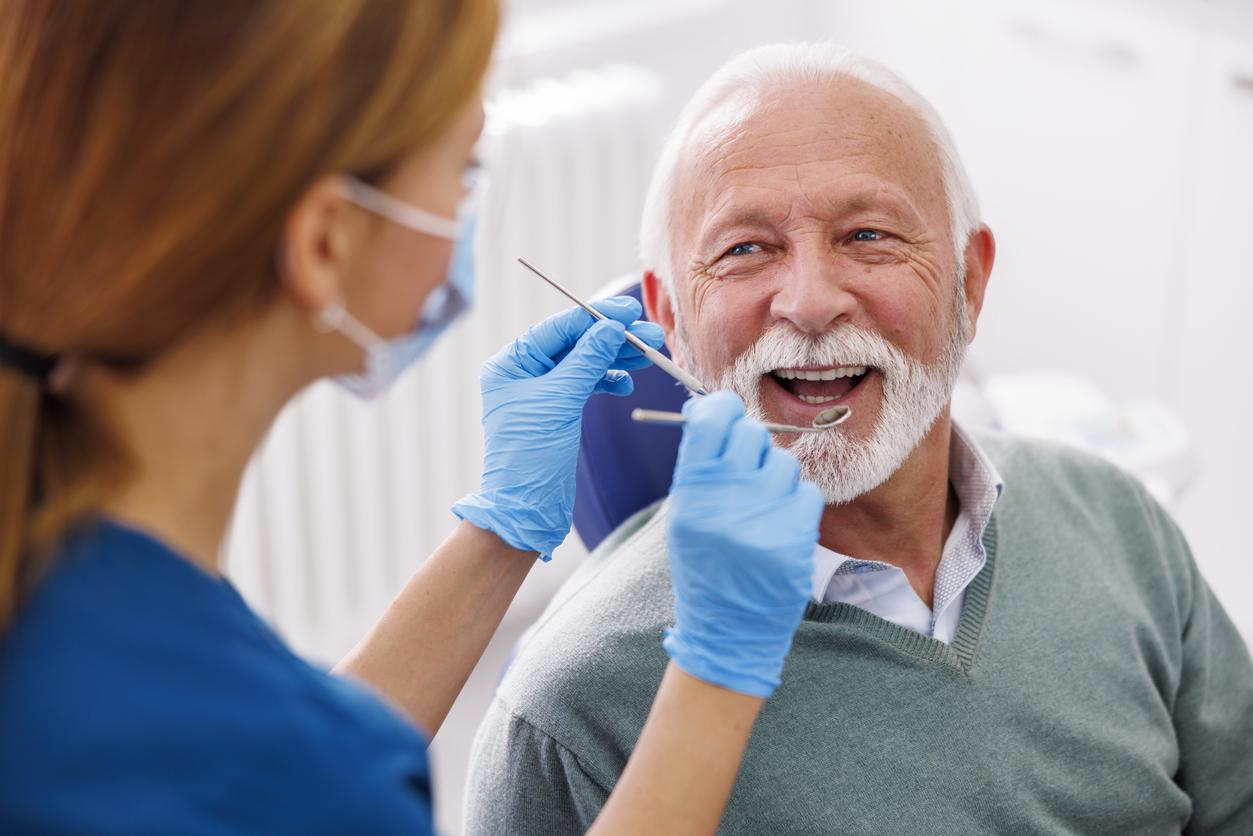 Mature man smiles as dental hygienist holds mirror and tools readying for a cleaning