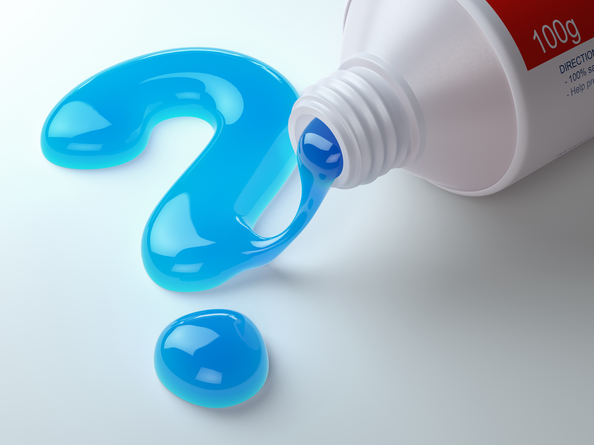 Red and white tube of toothpaste squirting out blue gel in the form of a question mark