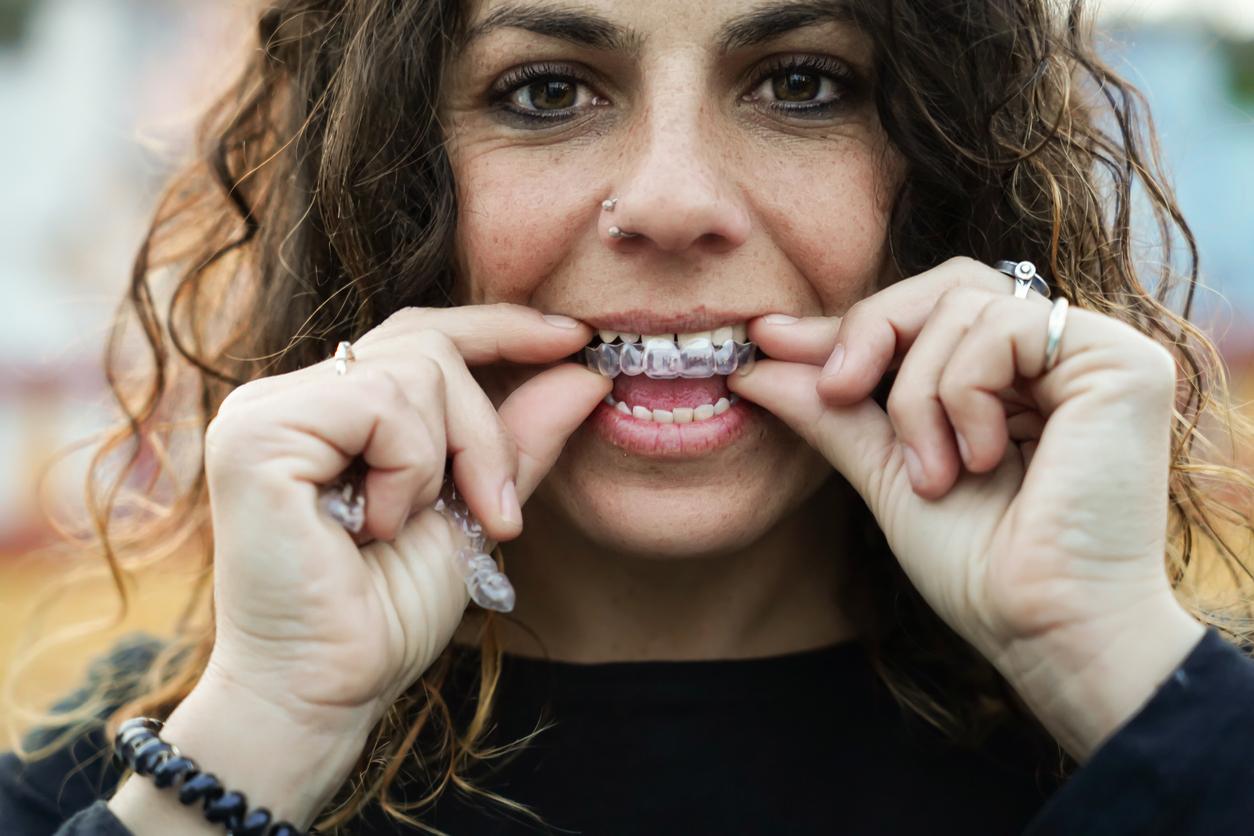 Woman with brown curly hair stands outside as she puts her invisible braces in