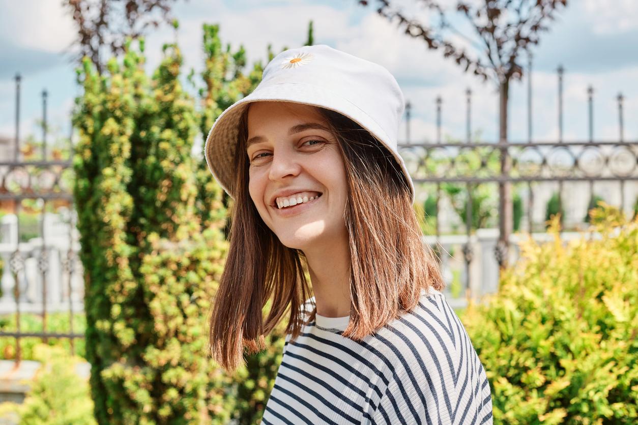 Teenage girl wearing bucket hat and striped shirt shares toothy smile with healthy teeth