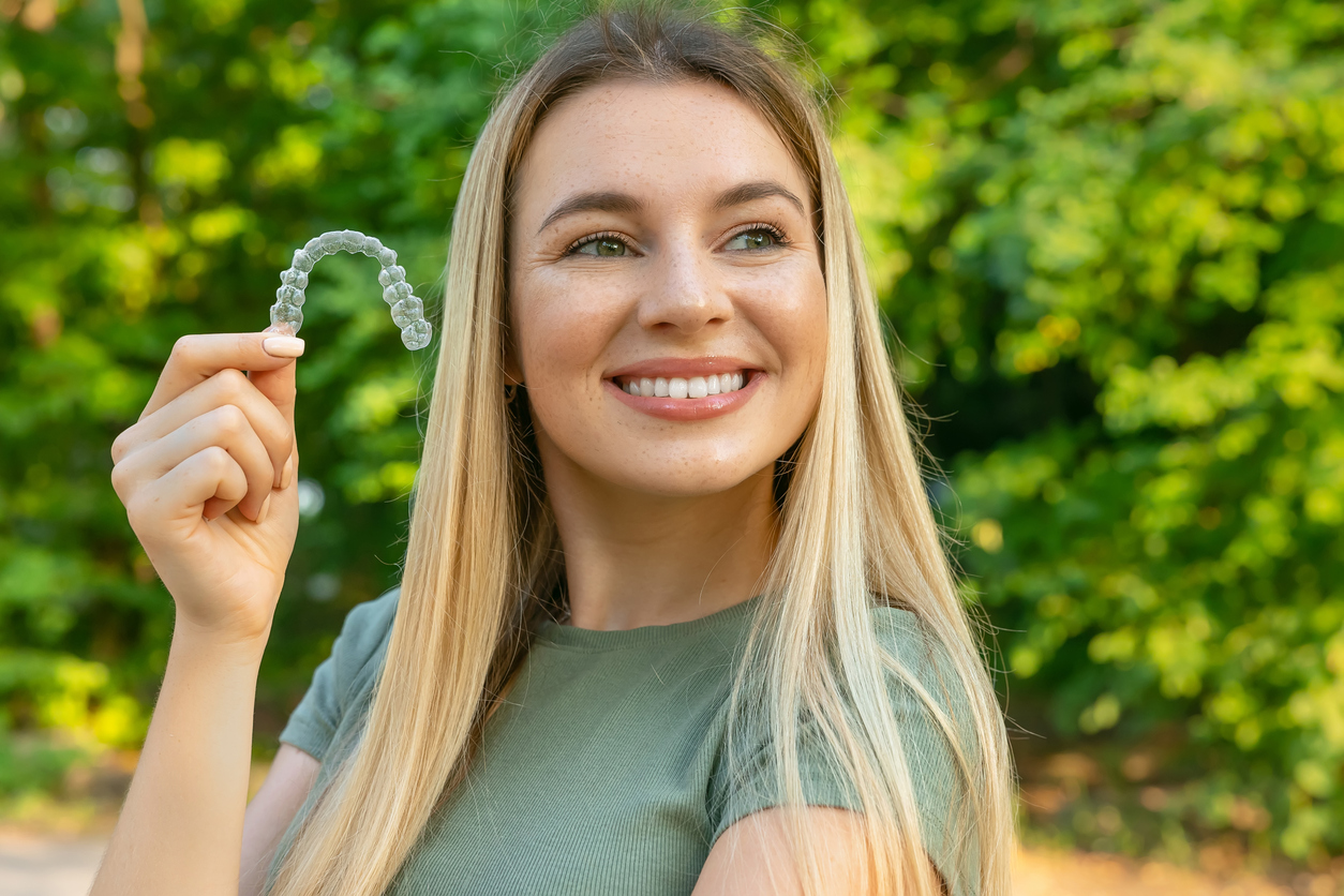 young beautiful woman smiling with hand holding dental aligner retainer (invisible) on green background