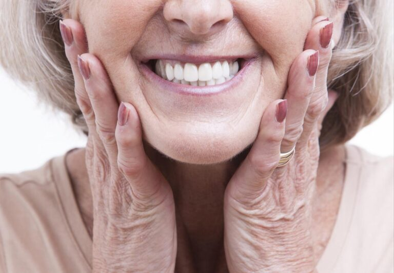 Older woman with dentures in Lakeview smiling and framing her face with her hands