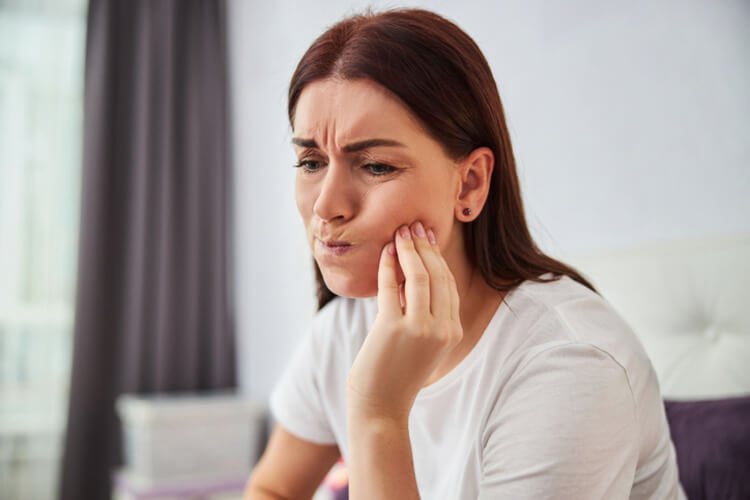 Woman touching her jaw and frowning in pain due to a broken tooth crown