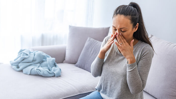 Woman with a cold causing sinus pressure and tooth pain pressing her fingers against her nose