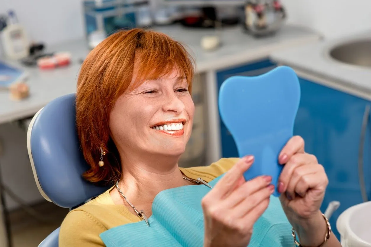 Patient smiling in mirror while in a dental chair after periodontal treatment
