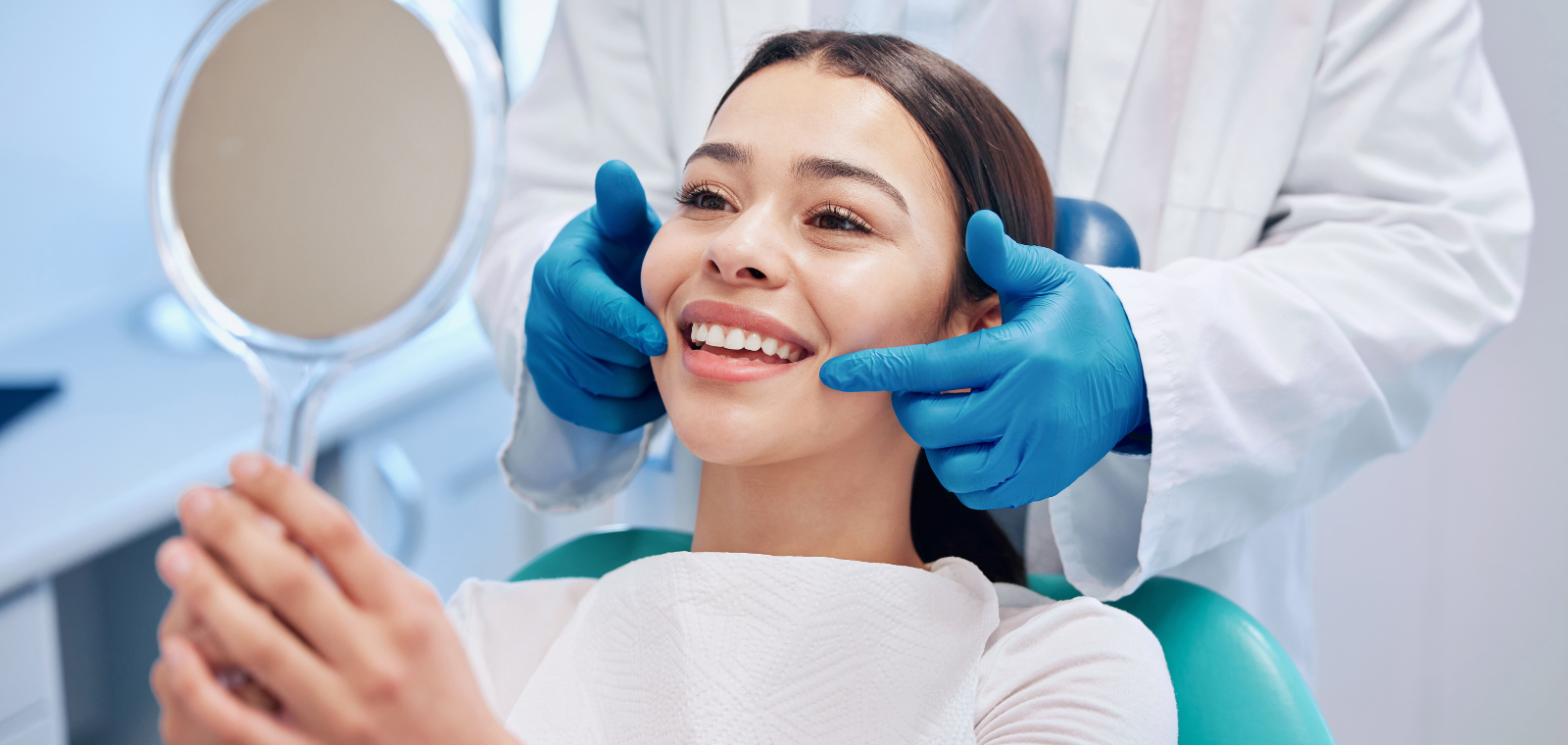 Patient admiring her restored smile in a hand mirror at the dental office